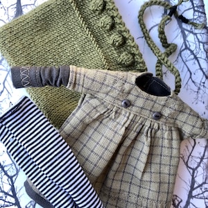 Puede incluir: Un vestido de punto verde con estampado de cuadros, un par de leggings a rayas blancas y negras y un gorro de punto verde con un cordón.