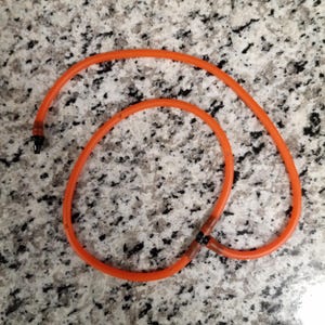 May include: An orange rubber tube, looped into a figure-eight shape, with a black tip on one end. The tube is lying on a speckled, light gray surface.