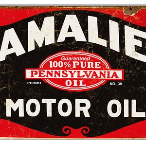 May include: Vintage metal sign advertising Amalie Motor Oil. The sign features a red and black color scheme with white text. The text reads "Amalie" in a large, bold font, followed by "Guaranteed 100% Pure Pennsylvania Oil" in a smaller font within a circle. The bottom of the sign reads "Motor Oil" in a large, bold font.