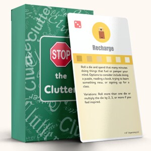 May include: A green box with the words "Stop the Clutter" on it. A white card with the words "Recharge" and a battery icon is next to the box. The card has instructions to roll a die and spend that many minutes doing things that fuel or pamper your mind.  The card also includes variations on how to play the game.