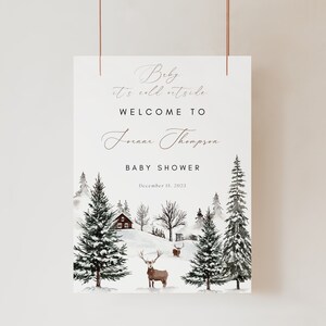 K&ouml;nnte beinhalten: Ein Willkommens-Schild f&uuml;r eine Babyparty im Winterwunderland mit einer verschneiten Waldszene, einer roten H&uuml;tte und einem Reh. Der Text lautet "Baby it's cold outside, Welcome to [name] Thompson Baby Shower, December 15, 2023."