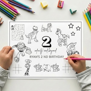May include: A black and white Toy Story themed coloring sheet with various characters, a maze, and tic-tac-toe grids. The text reads "2", "infinity and beyond", and "RYAN'S 2 ND BIRTHDAY". Colouring pencils are scattered around the page.