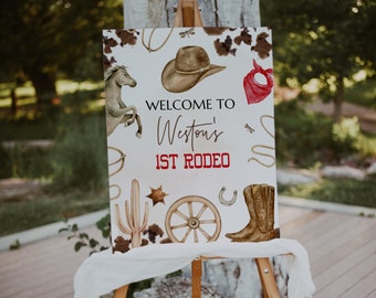 May include: Welcome to Weston's 1st Rodeo sign with a watercolor design. The sign features a cowboy hat, a lasso, a horseshoe, a cactus, a wagon wheel, a cowboy boot, and a red bandana.