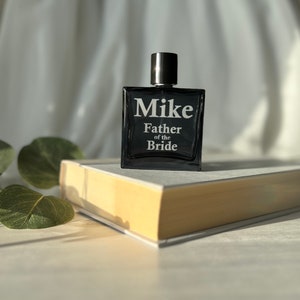 May include: A black glass bottle of cologne with a black cap. The bottle has the text "Mike Father of the Bride" printed on it.