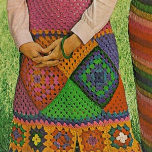 May include: A woman wearing a pink long-sleeve shirt and a colorful crochet skirt. The skirt features a patchwork design with squares of pink, orange, green, and purple. A green belt and a gold necklace complete the look.