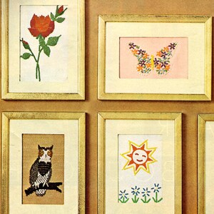 May include: A collection of framed cross-stitch art pieces. The pieces include a red rose, a butterfly made of flowers, an owl on a branch, and a smiling sun with flowers. The frames are gold-colored.