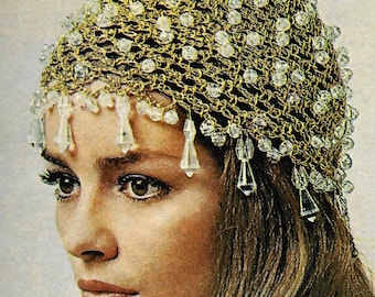 May include: A gold-toned crocheted head covering adorned with clear, sparkling beads. The headpiece features a delicate net-like design, with dangling crystal-like accents along the forehead. The overall style is reminiscent of vintage fashion.