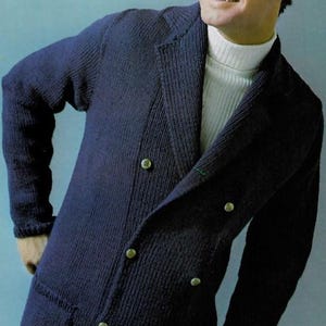 May include: A navy blue knit blazer with a double-breasted design. The blazer features gold-colored buttons and two front pockets. The person in the image is wearing a white turtleneck underneath and sunglasses.