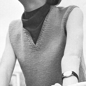 Peut inclure: Image en noir et blanc d'un gilet tricoté avec un col en V, porté sur un col roulé foncé. Le gilet est de couleur claire, peut-être beige ou gris. Une montre-bracelet avec un bracelet foncé est visible sur le bras. La personne tient un guidon de vélo.