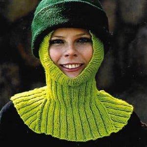 Peut inclure: Une cagoule verte tricotée avec un bonnet vert assorti. La cagoule présente une texture côtelée autour du cou et de l'ouverture du visage. La personne porte un haut noir.