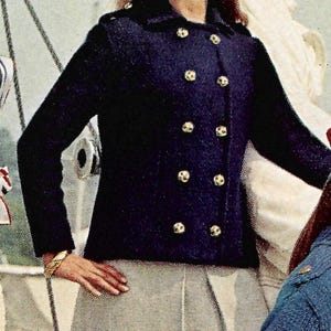 May include: A navy blue double-breasted jacket with gold buttons and a gray skirt. The jacket has long sleeves and a classic design. The woman is wearing sunglasses on her head and gold jewelry.