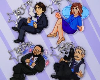 May include: Four character-themed keychains. Each keychain features a cartoon illustration of a person in business attire. The keychains have silver star-shaped charms and key rings. The background is a light purple color.