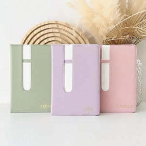 May include: Three pastel-colored journals with white accents and personalized names. The journals are in shades of green, lavender, and pink. The names "Emma", "Lisa", and "Camille" are printed in gold on the lower right corner.