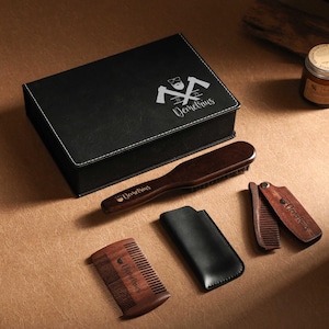 May include: A black leatherette box with the name "Demetrius" and a logo, along with a wooden beard brush, combs, and a leather case. A jar of beard balm is also visible. The items are arranged on a brown surface.