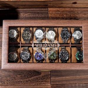 May include: A wooden watch box with a glass top, displaying 12 watches. The box has a personalized inscription that reads "WILLIAMS".