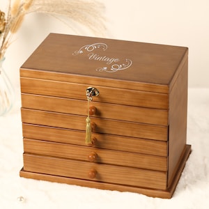 May include: A wooden jewellery box with five drawers and a gold-coloured lock and tassel. The top drawer has the word "Vintage" engraved on it.