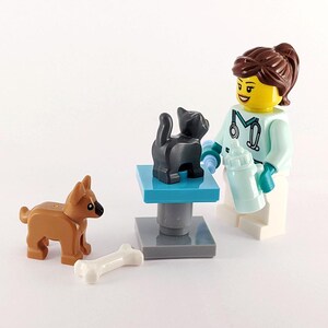 May include: A female Lego minifigure wearing a white lab coat with a stethoscope and a green shirt is holding a blue bottle. A black cat is on a blue examination table. A brown dog and a white bone are on the floor.