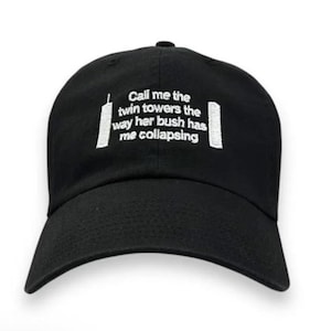 Puede incluir: Gorra de béisbol negra con texto y gráficos bordados en blanco. El texto dice: "Llámame las torres gemelas como su arbusto me ha hecho colapsar." Los gráficos son representaciones estilizadas de las Torres Gemelas.