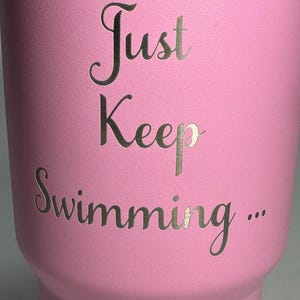 以下が含まれることがあります： 前面に「Just Keep Swimming... 」という文字が刻まれたピンク色のステンレス製タンブラーです。
