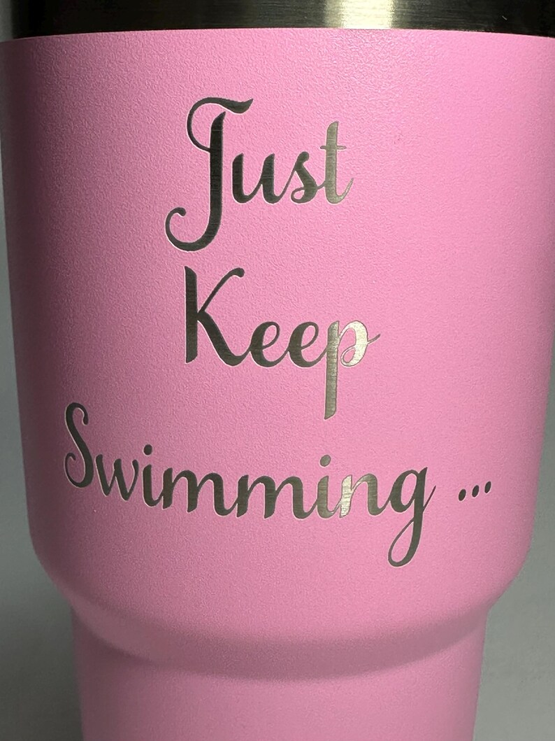 以下が含まれることがあります： 前面に「Just Keep Swimming... 」という文字が刻まれたピンク色のステンレス製タンブラーです。