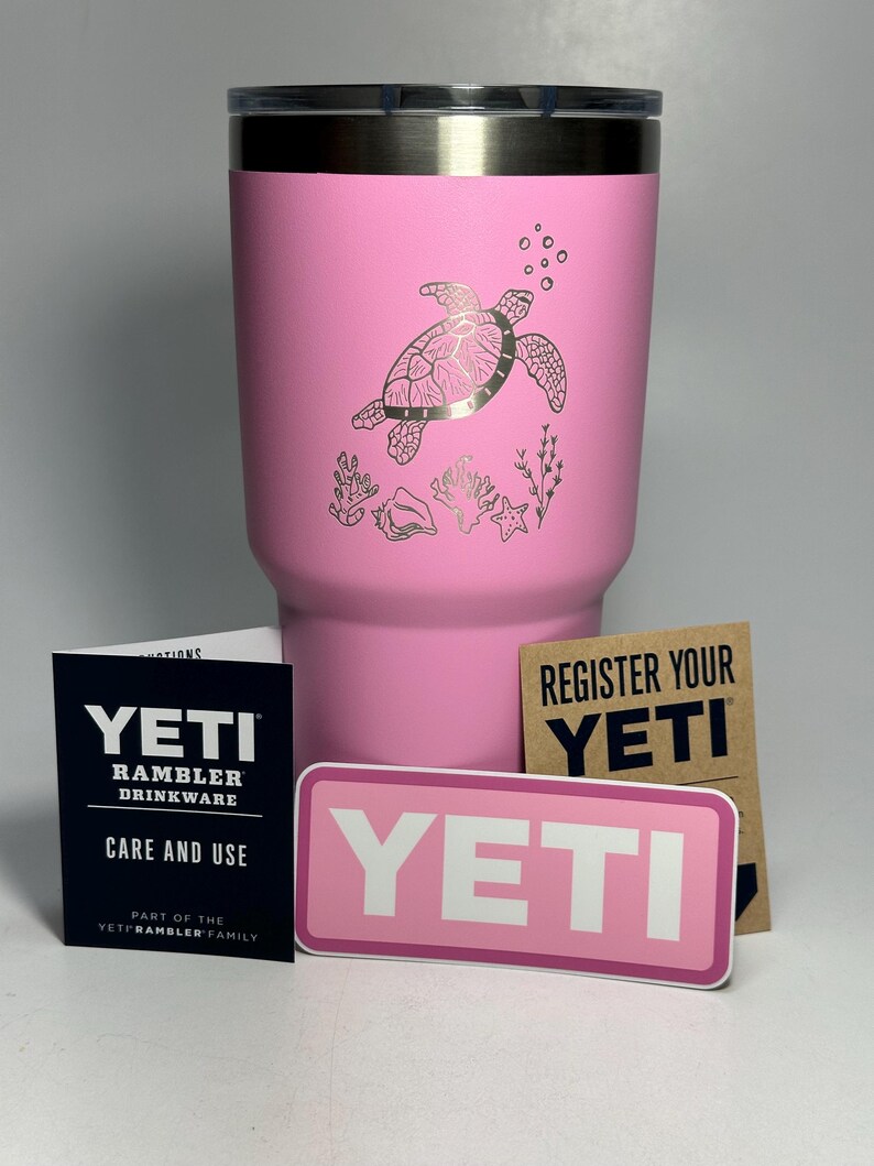以下が含まれることがあります： ピンクのYETIランブラータンブラーに、ウミガメのデザインが施されています。タンブラーにはステンレス製の蓋と「YETI」と書かれたステッカーが付いています。