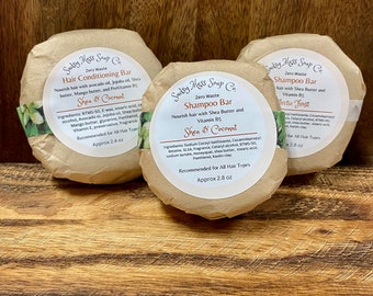 May include: Three brown paper-wrapped bars of soap with white text. The bars are labeled "Sudsy Mess Soap Co." and are for hair conditioning and shampoo. The shampoo bars are labeled "Shea & Coconut" and "Arctic Frost". The conditioning bar is labeled "Shea & Coconut".