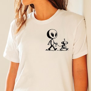 May include: White t-shirt with a black and white illustration of an alien walking a robot dog.