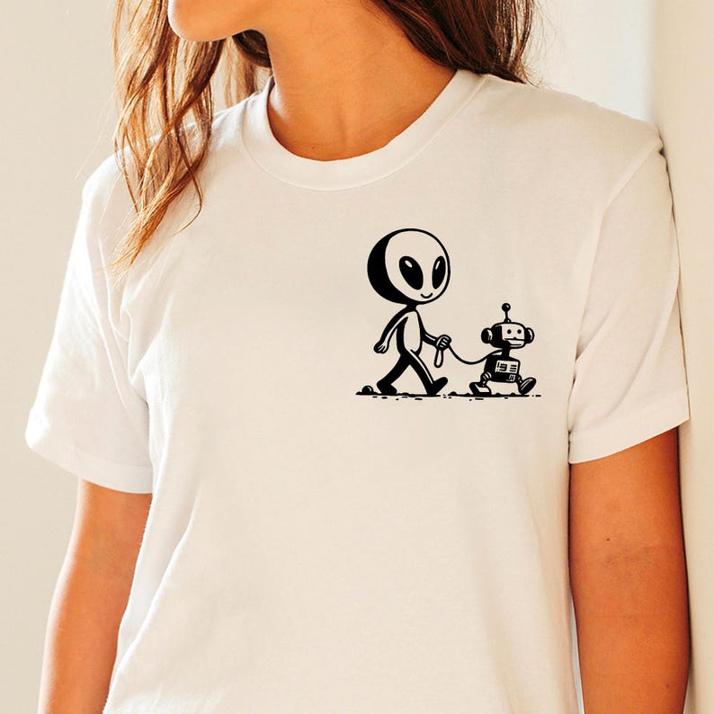 May include: White t-shirt with a black and white illustration of an alien walking a robot dog.