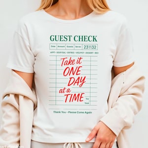 May include: White t-shirt with a green and white guest check design that says "Take it ONE DAY at a TIME".