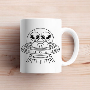 May include: White ceramic mug with a black and white illustration of two aliens in a flying saucer. The aliens have large eyes and are smiling.