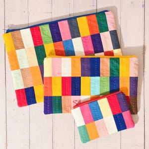 May include: Three colourful patchwork zippered pouches in different sizes. The largest pouch is blue, the medium pouch is yellow, and the smallest pouch is red. All three pouches have a patchwork design with squares of various colours, including red, yellow, blue, green, pink, and orange.