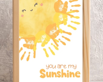 May include: A framed print with a yellow sun made from handprints. The sun has a smiling face and the text "you are my Sunshine" is below it.