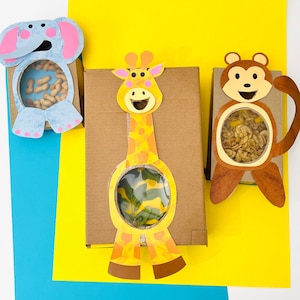 May include: Three cardboard boxes with animal cutouts on the front. The boxes are decorated with a giraffe, an elephant, and a monkey. Each box has a clear plastic window on the front, revealing a space for treats or small toys.