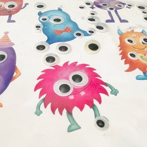 May include: A white sheet of paper with five colorful cartoon monsters with googly eyes. The monsters are pink, blue, purple, orange, and green. There are many googly eyes scattered around the monsters.
