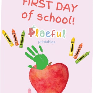 May include: A red apple with a green handprint on top. The text "FIRST DAY of school!" is written in red at the top of the image. The text "Playful printables" is written in blue and pink at the bottom of the image. There are crayons in the image.