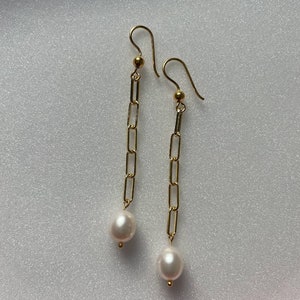May include: Gold chain earrings with a white pearl dangling at the end of each chain.