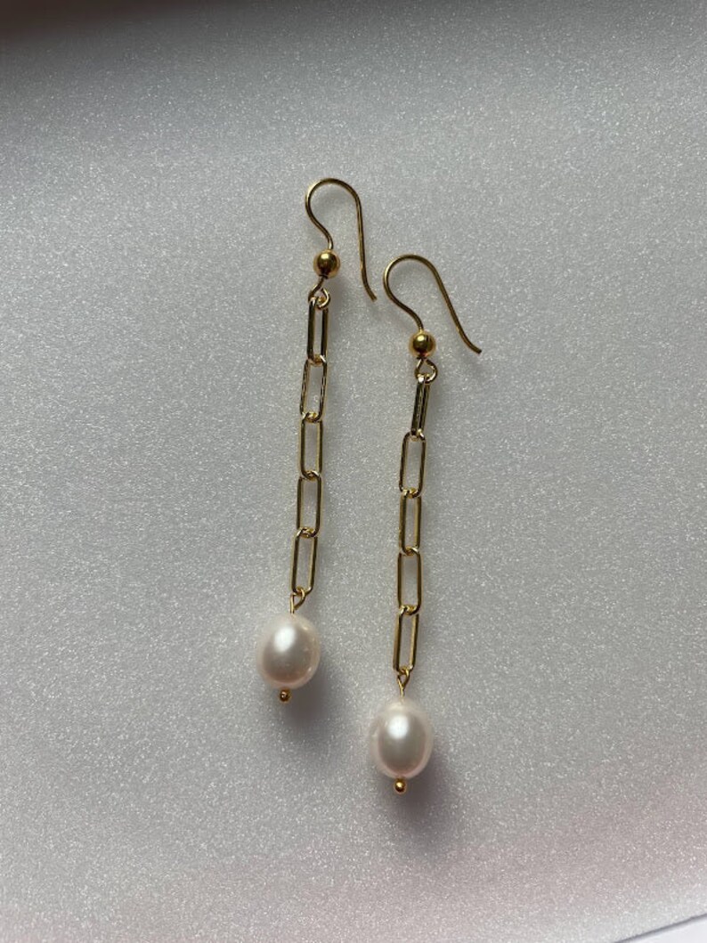 May include: Gold chain earrings with a white pearl dangling at the end of each chain.