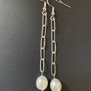 May include: A pair of silver chain earrings with a white pearl dangling from each chain.