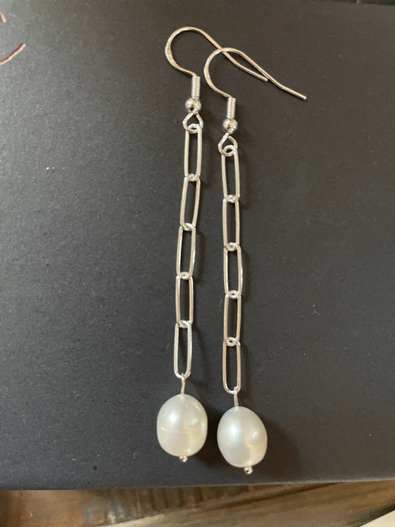 May include: A pair of silver chain earrings with a white pearl dangling from each chain.
