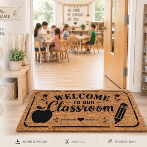 Può includere: Uno zerbino rettangolare in fibra di cocco marrone con un design stampato in nero che riporta il testo WELCOME TO OUR CLASSROOM, un'icona a forma di mela, una matita, stelle e un cuore. Il tappetino è posto davanti a una porta aperta.