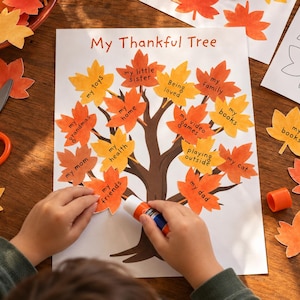 May include: A My Thankful Tree craft project on white paper featuring a brown tree trunk and orange and yellow paper leaves with handwritten text including my toys, my little sister, being loved, my family, my books, my home, my video games, my health, playing outside, my cat, my mom, my friends, and my dad.