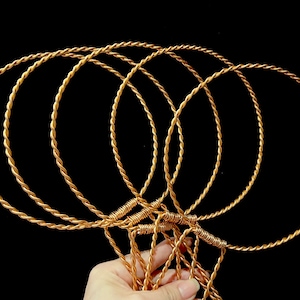 May include: Five gold-colored wire hoops, each with a twisted design, are held together at the bottom. The hoops are all the same size and are arranged in a fan shape.