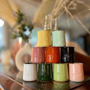 May include: A stack of nine ceramic jars in various colors, including yellow, green, red, black, and white. Each jar has the words "la famille" embossed on the side.