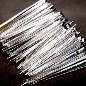 May include: A pile of clear, iridescent glass rods, arranged in a fan shape. The rods are approximately 6 inches long and have a rectangular cross-section.