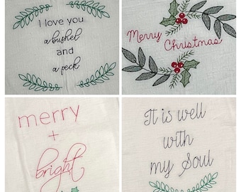 May include: Four white fabric squares with embroidered text and designs. One says "I love you a bushel and a peck" with green leaf accents. Another says "Merry Christmas" with holly and leaves. A third says "merry + bright" with holly. The last says "It is well with my soul".