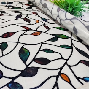 May include: A stained glass window film with a design of leaves in various colors, including green, red, orange, and blue. The film is rolled up and ready to be applied to a window.