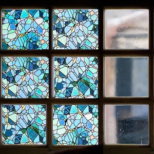 May include: A window with six panes of glass. The top three panes feature a blue and green stained glass design. The bottom three panes are clear glass.