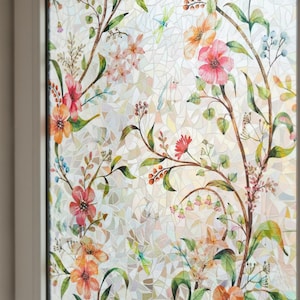 Pu&ograve; includere: Una pellicola decorativa per finestre con un design floreale. Presenta fiori in stile acquerello nei toni dell'arancione, rosa e rosso, insieme a foglie e steli verdi. Lo sfondo ha un motivo a mosaico.