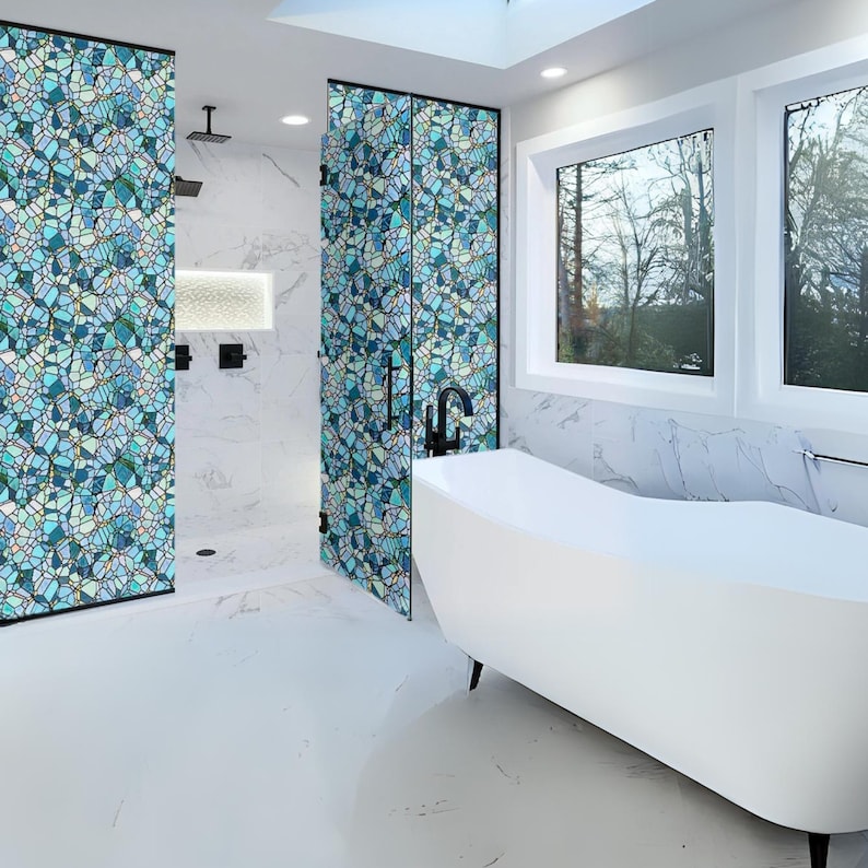 May include: A white bathtub with a curved design sits in a bathroom with white marble walls and a shower with a blue and green mosaic tile pattern.