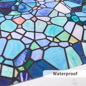 May include: A close-up of a blue and green stained glass window film with a waterproof label. The film has a textured surface and is designed to look like a stained glass window.